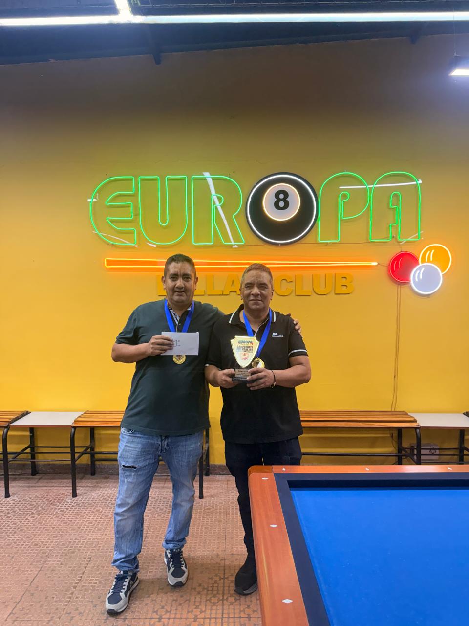 Pareja campeona del Campeonato por Parejas 2026 con trofeo y medallas frente al logo de Europa Billar Club